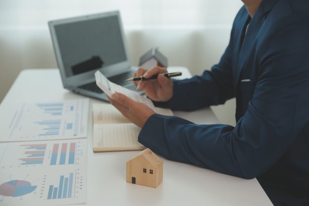 Profissional analisando cálculos financeiros com maquete de casa representando consórcio como investimento patrimonial