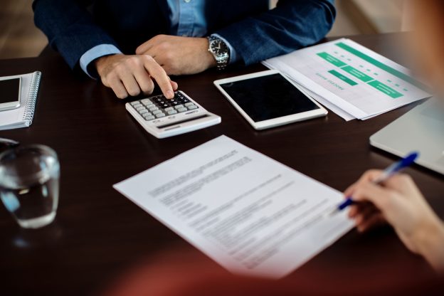 Pessoa analisando documentos financeiros e calculadora durante negociação para vender consórcio urgente com pagamento à vista.